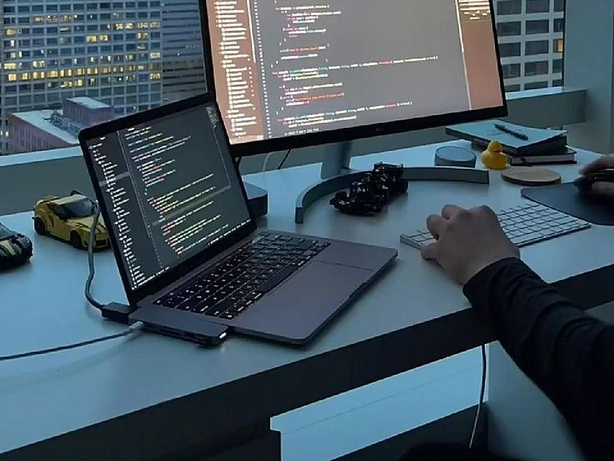 Developer coding on laptop and monitor with city view